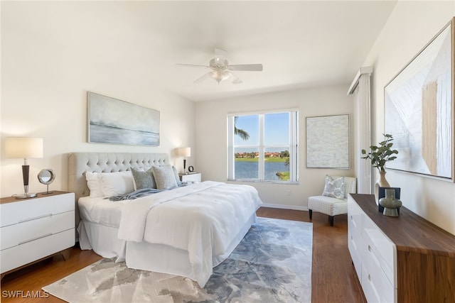 bedroom featuring dark hardwood / wood-style floors, ceiling fan, and a water view