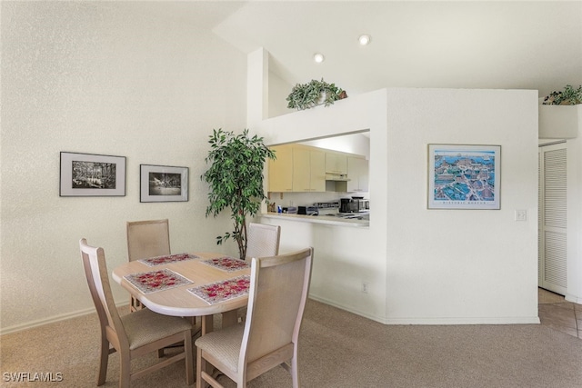 dining space with high vaulted ceiling and light carpet