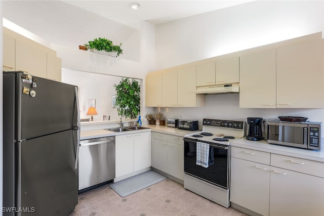 kitchen featuring a towering ceiling, appliances with stainless steel finishes, sink, and cream cabinetry