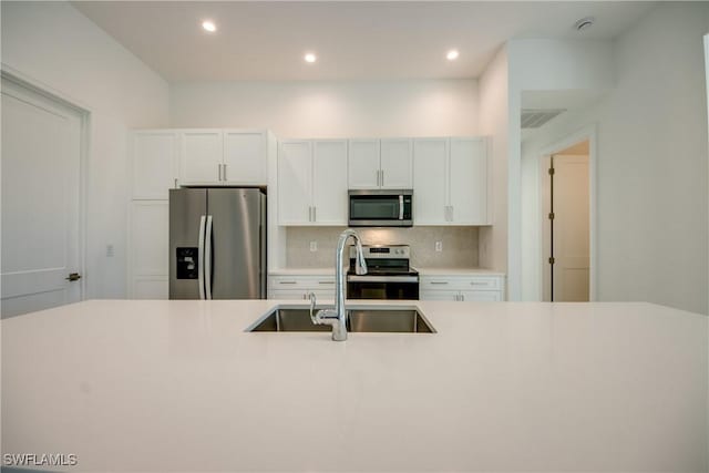 kitchen with sink, backsplash, white cabinets, and appliances with stainless steel finishes