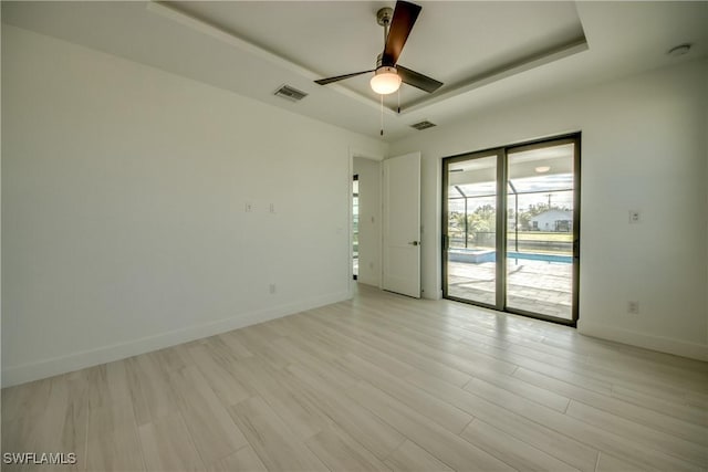 unfurnished room with a tray ceiling, light hardwood / wood-style floors, and ceiling fan