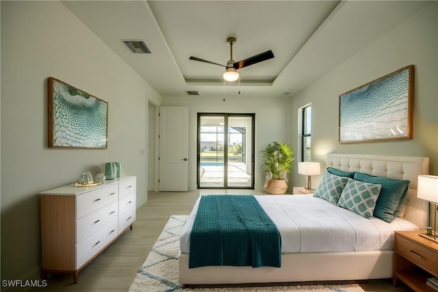 bedroom with a raised ceiling, access to exterior, ceiling fan, and light hardwood / wood-style floors