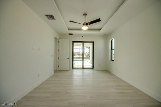 empty room with ceiling fan, a raised ceiling, and light hardwood / wood-style flooring