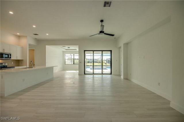 unfurnished living room with ceiling fan, sink, and light wood-type flooring