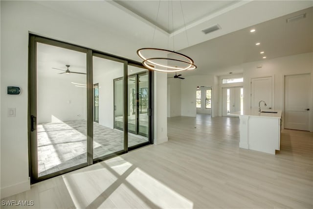 unfurnished room featuring ceiling fan with notable chandelier, sink, light hardwood / wood-style flooring, and a tray ceiling