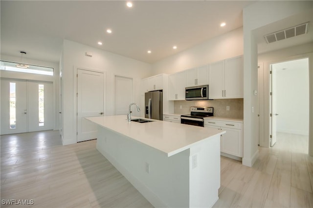 kitchen with white cabinetry, sink, stainless steel appliances, and an island with sink