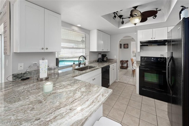 kitchen with under cabinet range hood, a tray ceiling, arched walkways, black appliances, and a sink