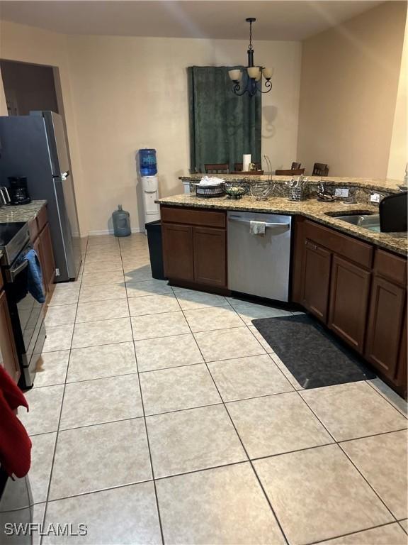 kitchen with light tile patterned floors, sink, dark stone countertops, stainless steel appliances, and decorative light fixtures