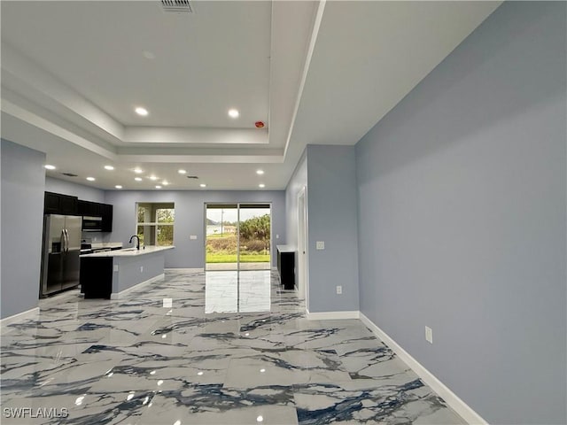 kitchen featuring sink, a tray ceiling, an island with sink, and appliances with stainless steel finishes