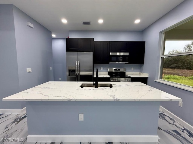 kitchen featuring a kitchen island with sink, sink, light stone counters, and appliances with stainless steel finishes