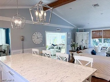 kitchen featuring pendant lighting, white cabinetry, vaulted ceiling with beams, an inviting chandelier, and a kitchen breakfast bar