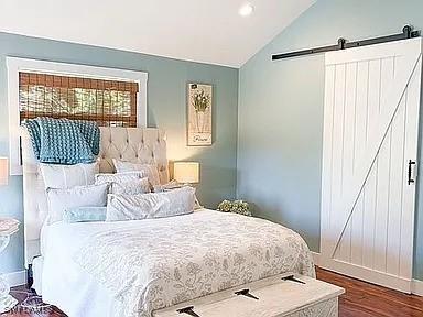 bedroom featuring dark hardwood / wood-style floors, vaulted ceiling, and a barn door