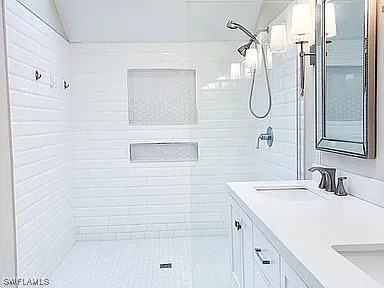 bathroom with lofted ceiling, vanity, and a tile shower