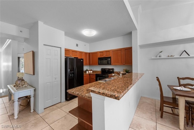 kitchen with light tile patterned flooring, black appliances, sink, dark stone counters, and kitchen peninsula