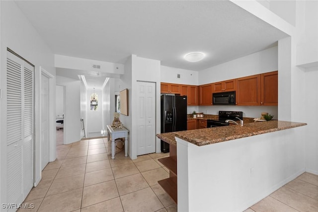 kitchen featuring dark stone countertops, kitchen peninsula, light tile patterned floors, and black appliances