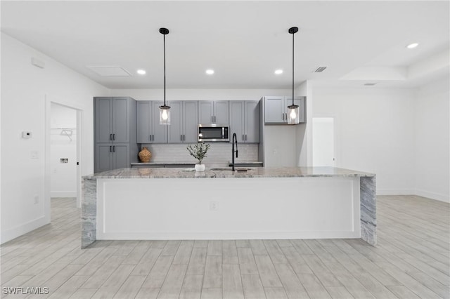 kitchen featuring light stone countertops, a kitchen island with sink, pendant lighting, and sink