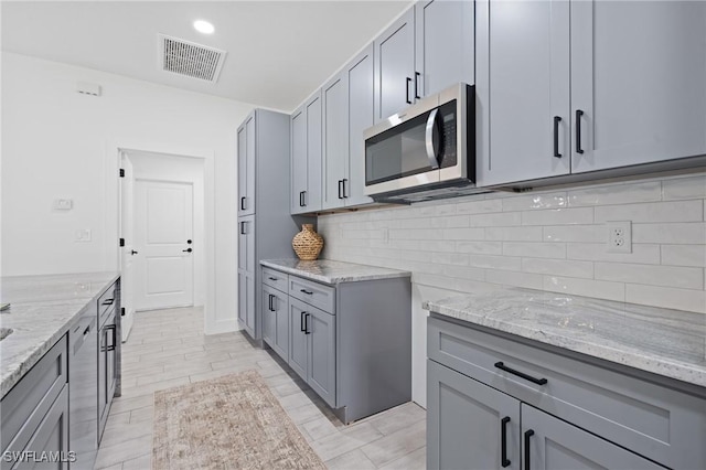 kitchen featuring tasteful backsplash, light stone countertops, and gray cabinetry