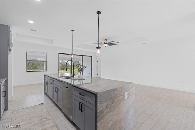 kitchen with gray cabinets, pendant lighting, sink, light stone counters, and a center island with sink