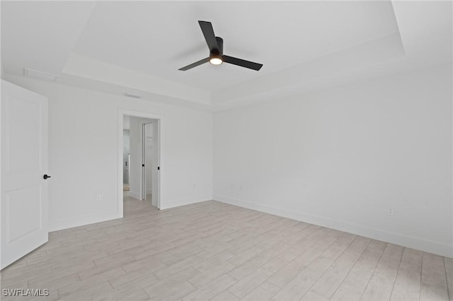 empty room featuring a tray ceiling, light hardwood / wood-style flooring, and ceiling fan