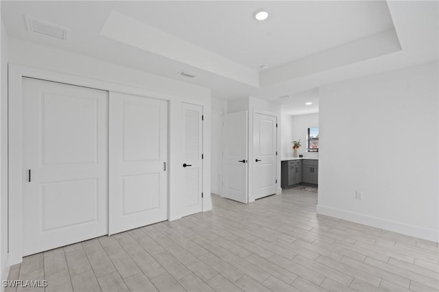 unfurnished bedroom featuring a closet, connected bathroom, light wood-type flooring, and a tray ceiling