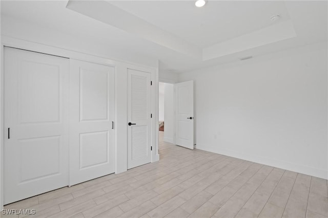 unfurnished bedroom with a tray ceiling, a closet, and light wood-type flooring