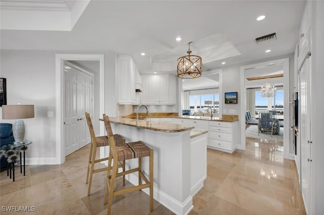 kitchen featuring a peninsula, an inviting chandelier, visible vents, and white cabinets