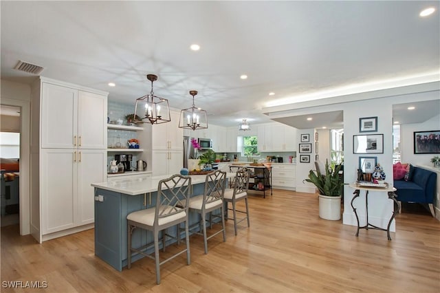 kitchen with a kitchen island, decorative light fixtures, white cabinets, stainless steel appliances, and light wood-type flooring