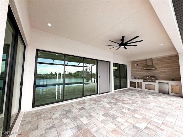 view of patio / terrace with area for grilling, a water view, ceiling fan, and an outdoor kitchen