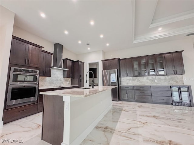 kitchen featuring sink, a center island with sink, wall chimney range hood, stainless steel appliances, and backsplash