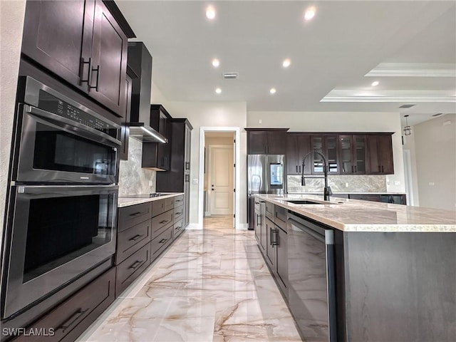 kitchen with an island with sink, appliances with stainless steel finishes, backsplash, and wall chimney exhaust hood