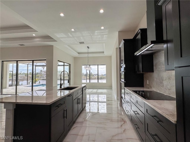 kitchen featuring sink, wall chimney range hood, appliances with stainless steel finishes, a spacious island, and a tray ceiling