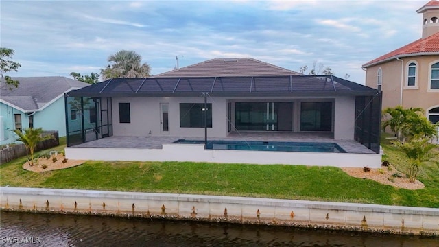 rear view of property with a water view, a lanai, a patio area, and a lawn