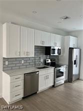 kitchen with white cabinetry, backsplash, stainless steel appliances, and light hardwood / wood-style floors