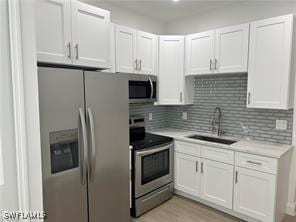 kitchen with stainless steel appliances, white cabinetry, sink, and tasteful backsplash