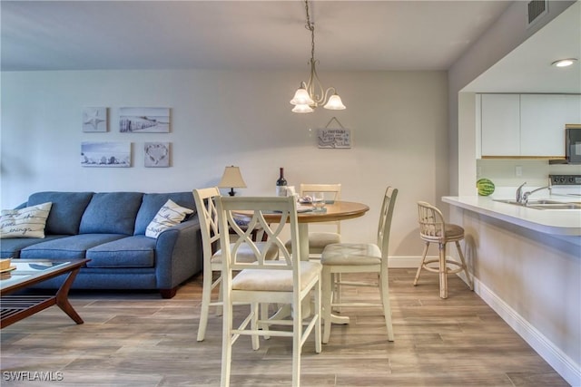 dining area with sink, a notable chandelier, and light wood-type flooring