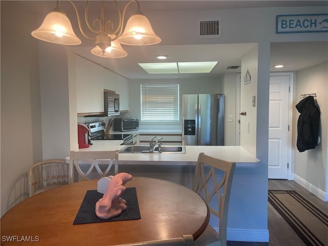 kitchen with dark wood-type flooring, sink, hanging light fixtures, appliances with stainless steel finishes, and kitchen peninsula