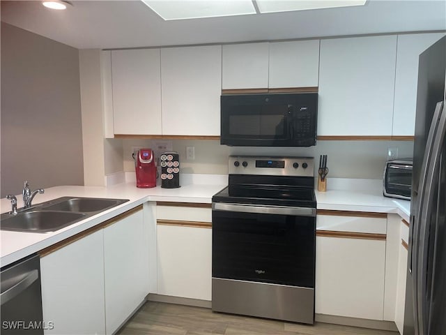 kitchen featuring sink, black appliances, white cabinets, and light wood-type flooring