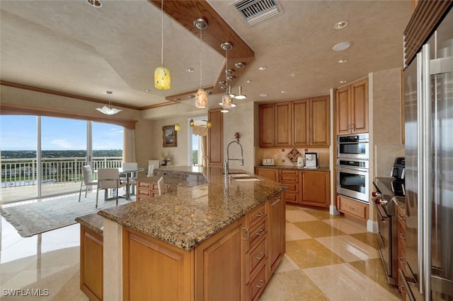 kitchen with pendant lighting, sink, light stone counters, and a large island with sink