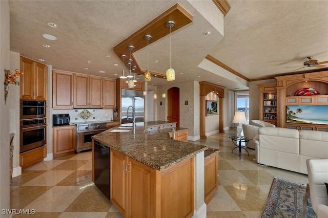 kitchen featuring sink, hanging light fixtures, dark stone countertops, premium appliances, and an island with sink