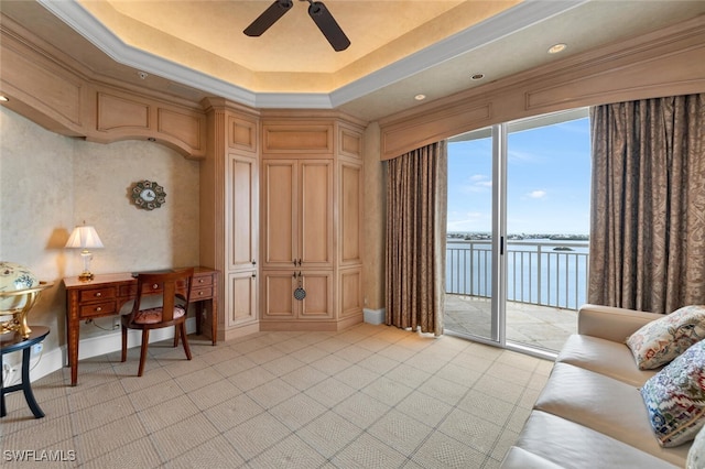 living area featuring a raised ceiling, a water view, and ceiling fan