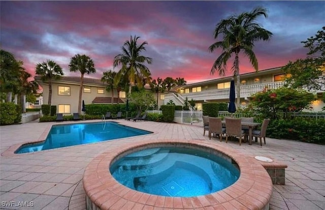 pool at dusk featuring a patio area and a hot tub