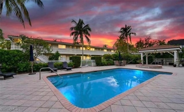 pool at dusk with an in ground hot tub, a patio area, and a gazebo