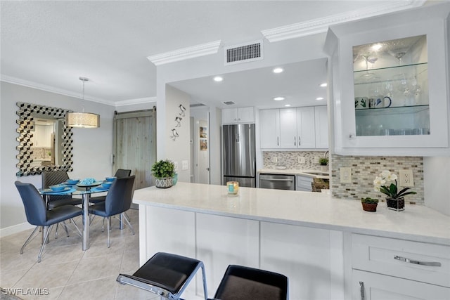 kitchen with decorative light fixtures, light tile patterned floors, stainless steel appliances, a barn door, and white cabinets