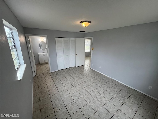 unfurnished bedroom with light tile patterned flooring, ensuite bath, and a closet