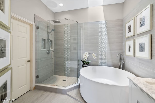 bathroom featuring vanity, independent shower and bath, and tile walls