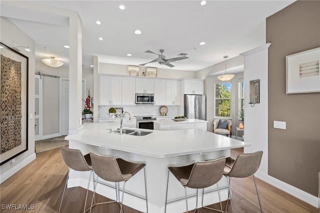 kitchen with sink, white cabinetry, decorative light fixtures, stainless steel appliances, and a barn door