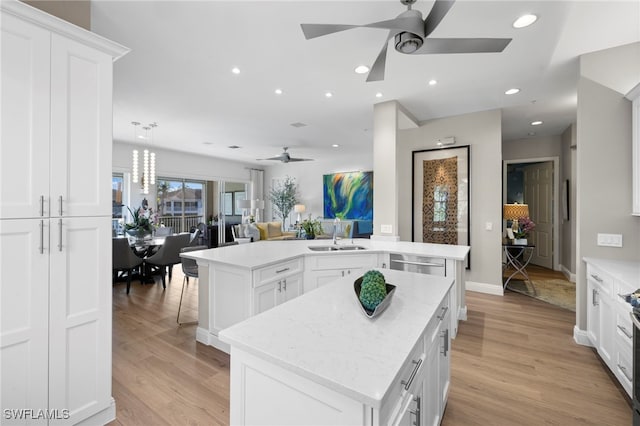 kitchen featuring a kitchen island with sink, sink, white cabinets, and light wood-type flooring