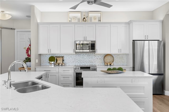 kitchen with sink, stainless steel appliances, light stone countertops, decorative backsplash, and white cabinets