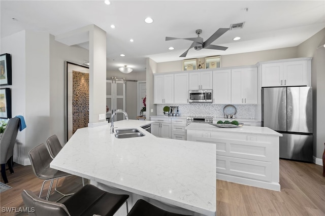 kitchen featuring a breakfast bar, sink, stainless steel appliances, a barn door, and white cabinets