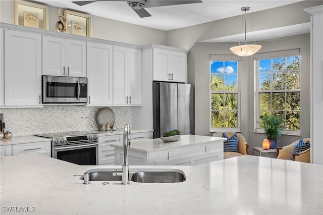 kitchen with pendant lighting, sink, stainless steel appliances, light stone countertops, and white cabinets